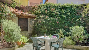 Une terrasse extérieure avec une table et des chaises, entourée d’une végétation luxuriante et d’un mur de pierre.