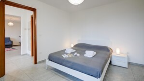 A modern bedroom with a neatly made bed, bedside lamps, and a visible door leading to another room. - Zio Enry Garden Orta Lake (Armeno)