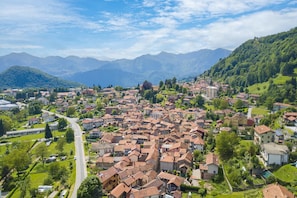 A town with a central road, surrounded by residential buildings and greenery, with mountains in the background. - Zio Enry Garden Orta Lake (Armeno)