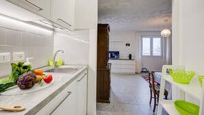 A modern kitchen with white cabinets, a marble countertop, and a sink. There is a dining area with a table and chairs visible in the background. - Zio Enry Garden Orta Lake (Armeno)
