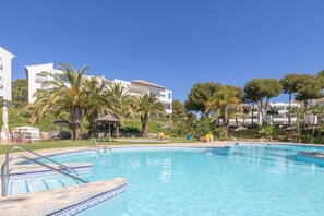 A swimming pool with clear blue water, surrounded by palm trees and a white building with balconies. - Rancho Miraflores Seaview Townhouse (Mijas)