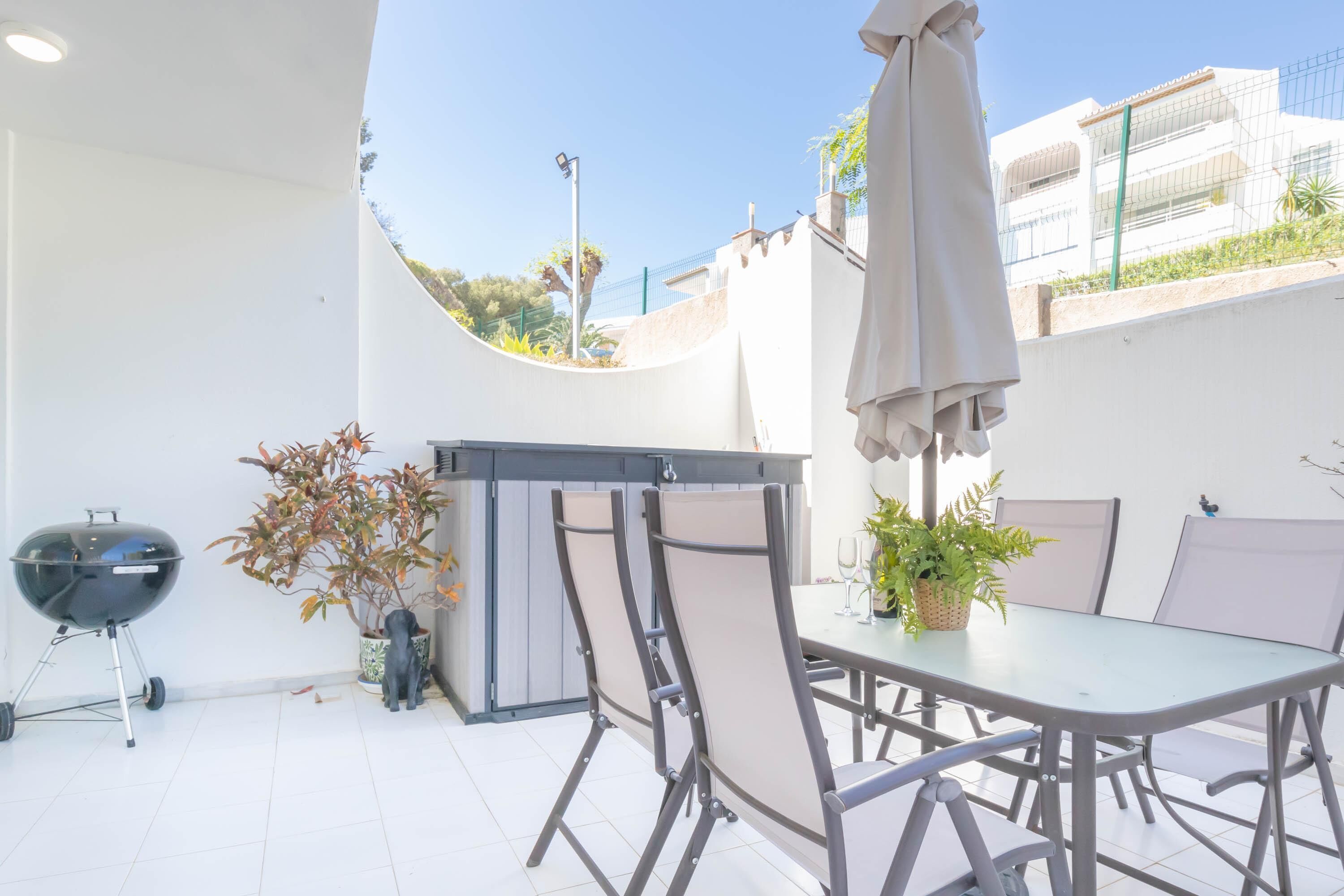 Une terrasse extérieure avec une table et des chaises, un barbecue et des plantes en pot.