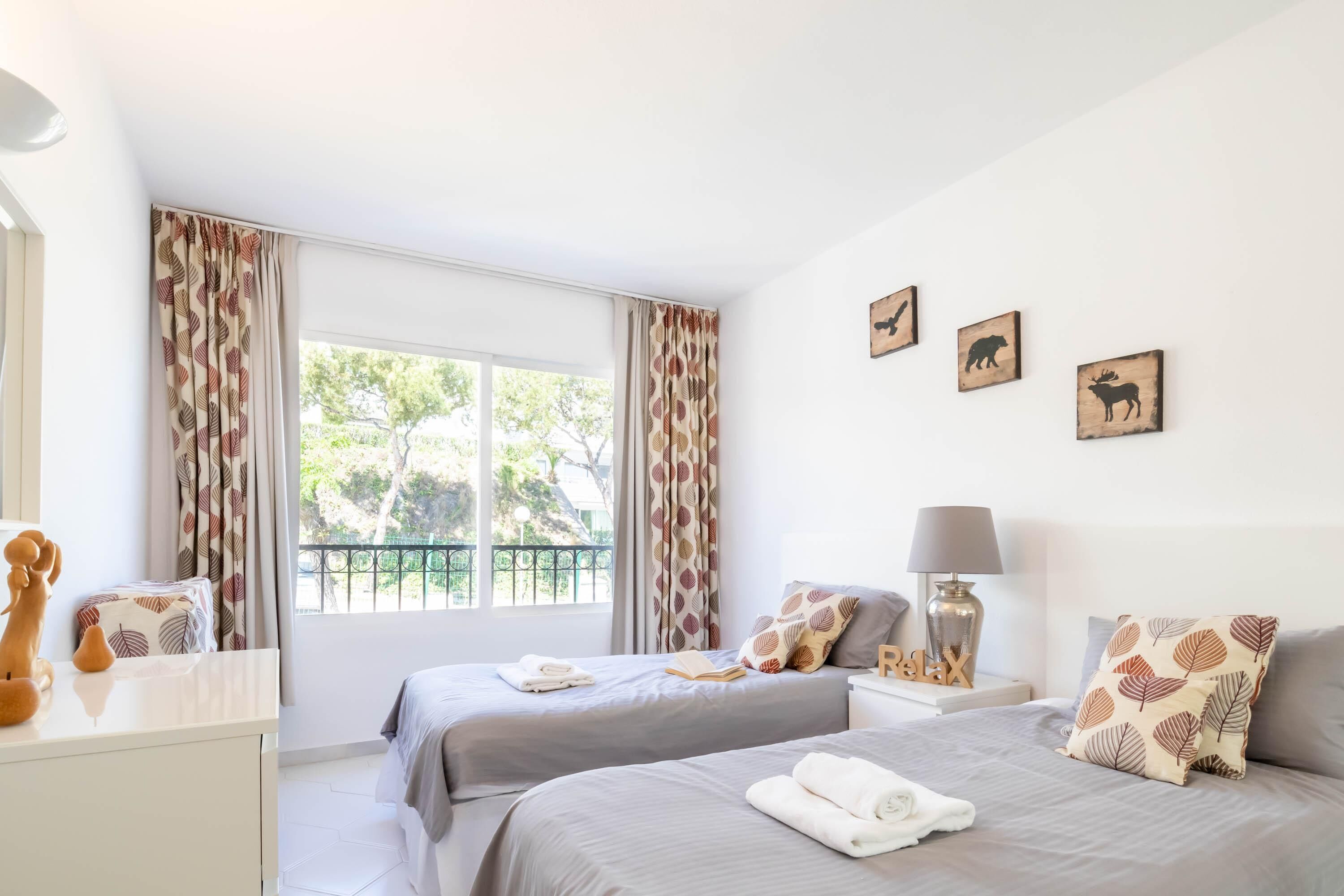 A bedroom with two beds, a nightstand, a lamp, and a window with curtains.