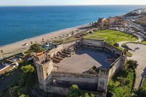 An aerial view of a coastal area with a historic fort, a beach, and modern buildings. - Cambural Beach Apartment (Fuengirola)