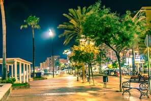A nighttime urban street with palm trees, benches, and a well-lit pedestrian walkway. - Cambural Beach Apartment (Fuengirola)