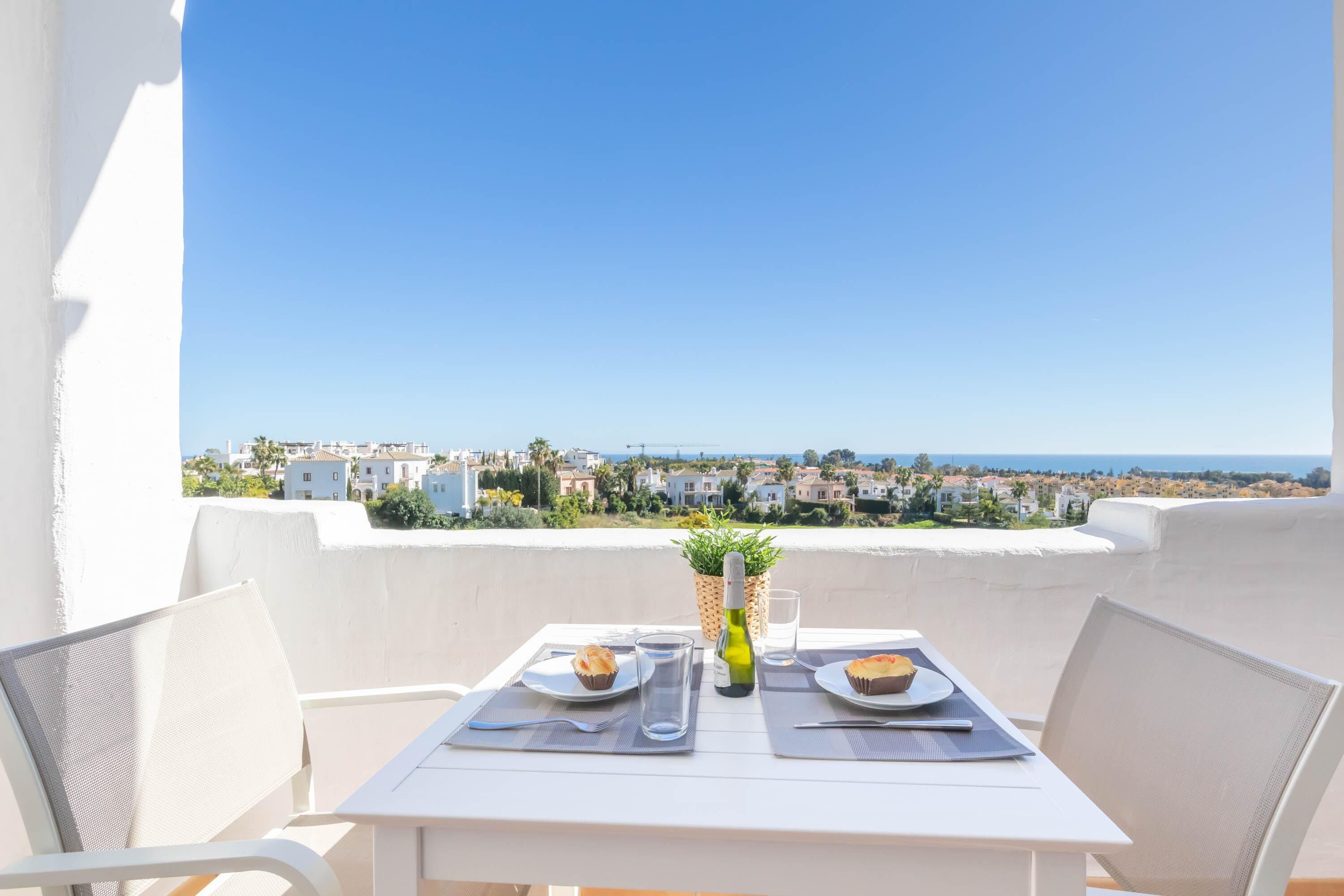 A balcony with a table set for two, overlooking a coastal town.