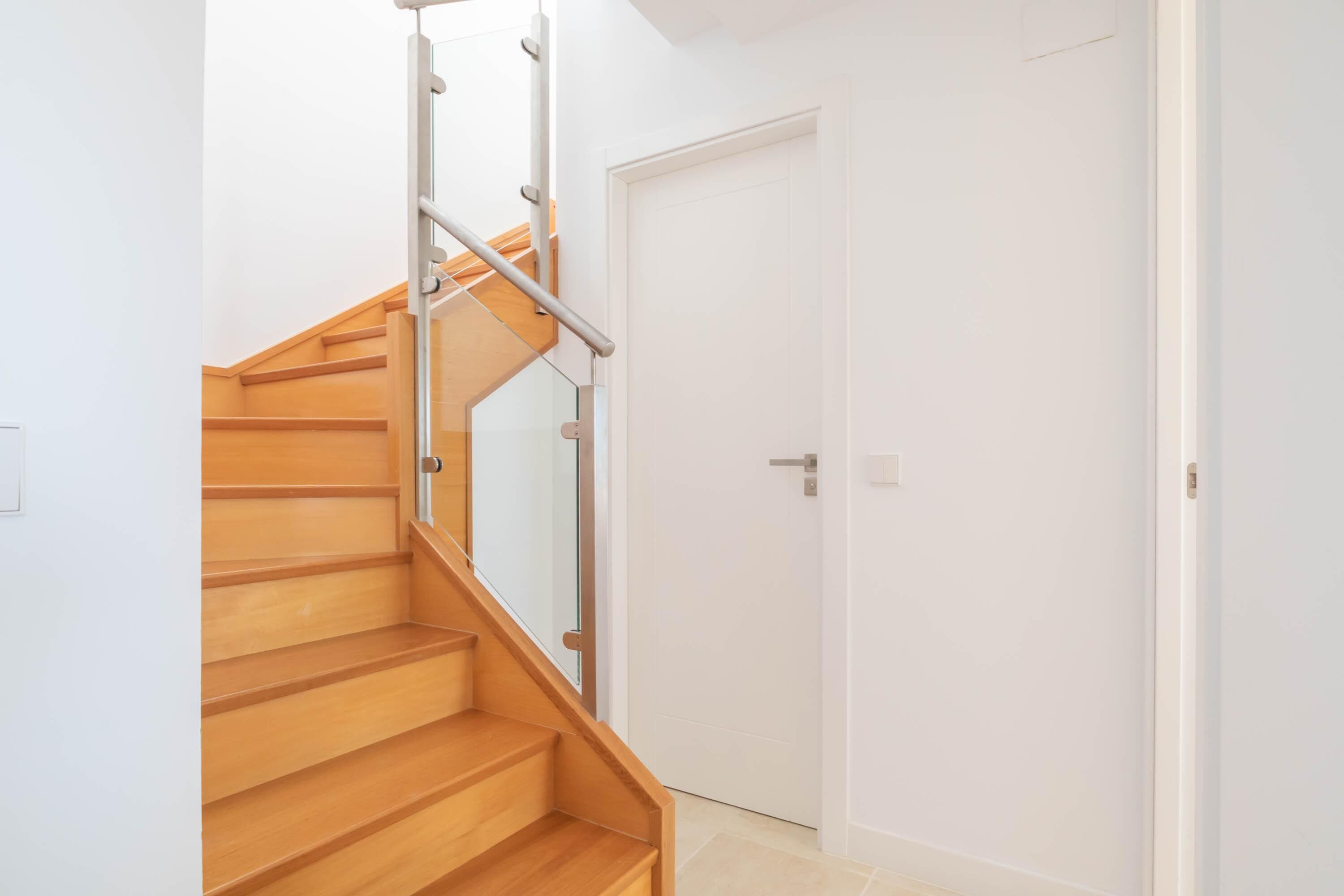 A staircase with wooden steps and a glass railing leading to a white door.