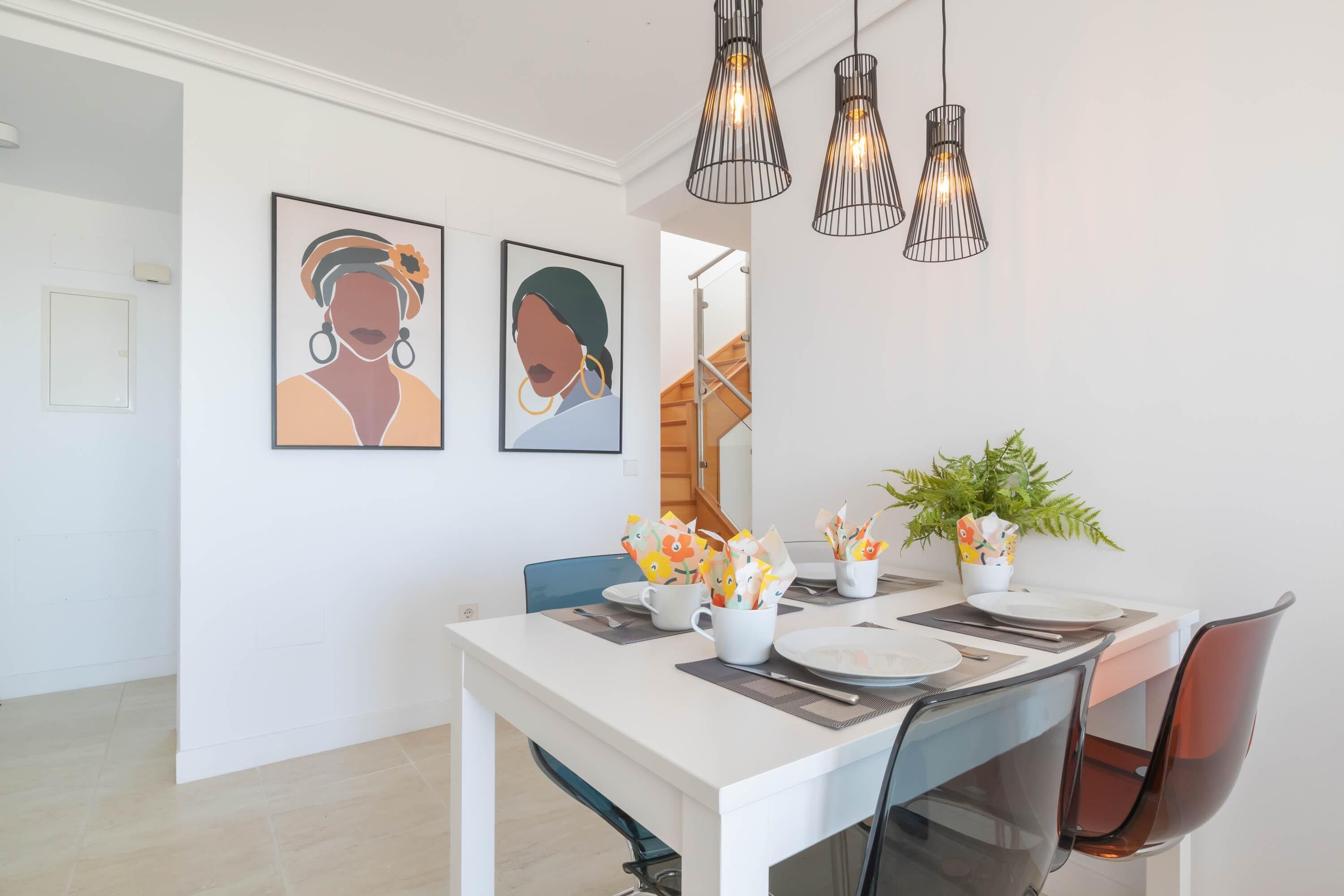 Un espace de salle à manger moderne avec une table blanche, des chaises noires et des luminaires suspendus.