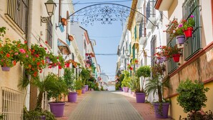 A narrow street lined with buildings, each adorned with potted plants and flowers. - Sunset Rama La Resina Golf (Estepona)