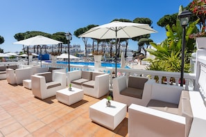 A rooftop pool area with white outdoor furniture, umbrellas, and a clear view of the pool.