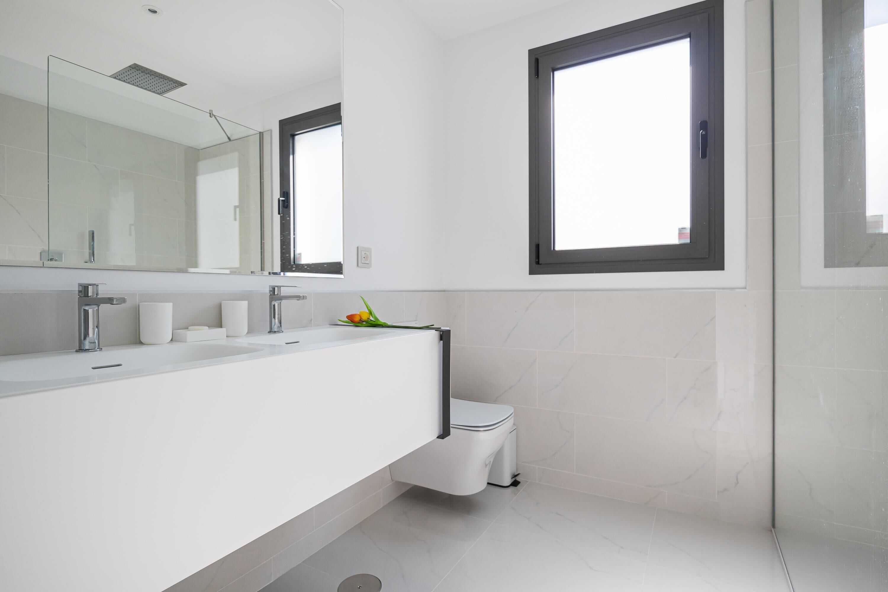 Une salle de bain moderne avec un grand miroir, deux lavabos, des toilettes et une fenêtre.