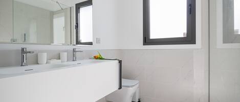 Une salle de bain moderne avec un grand miroir, deux lavabos, des toilettes et une fenêtre.