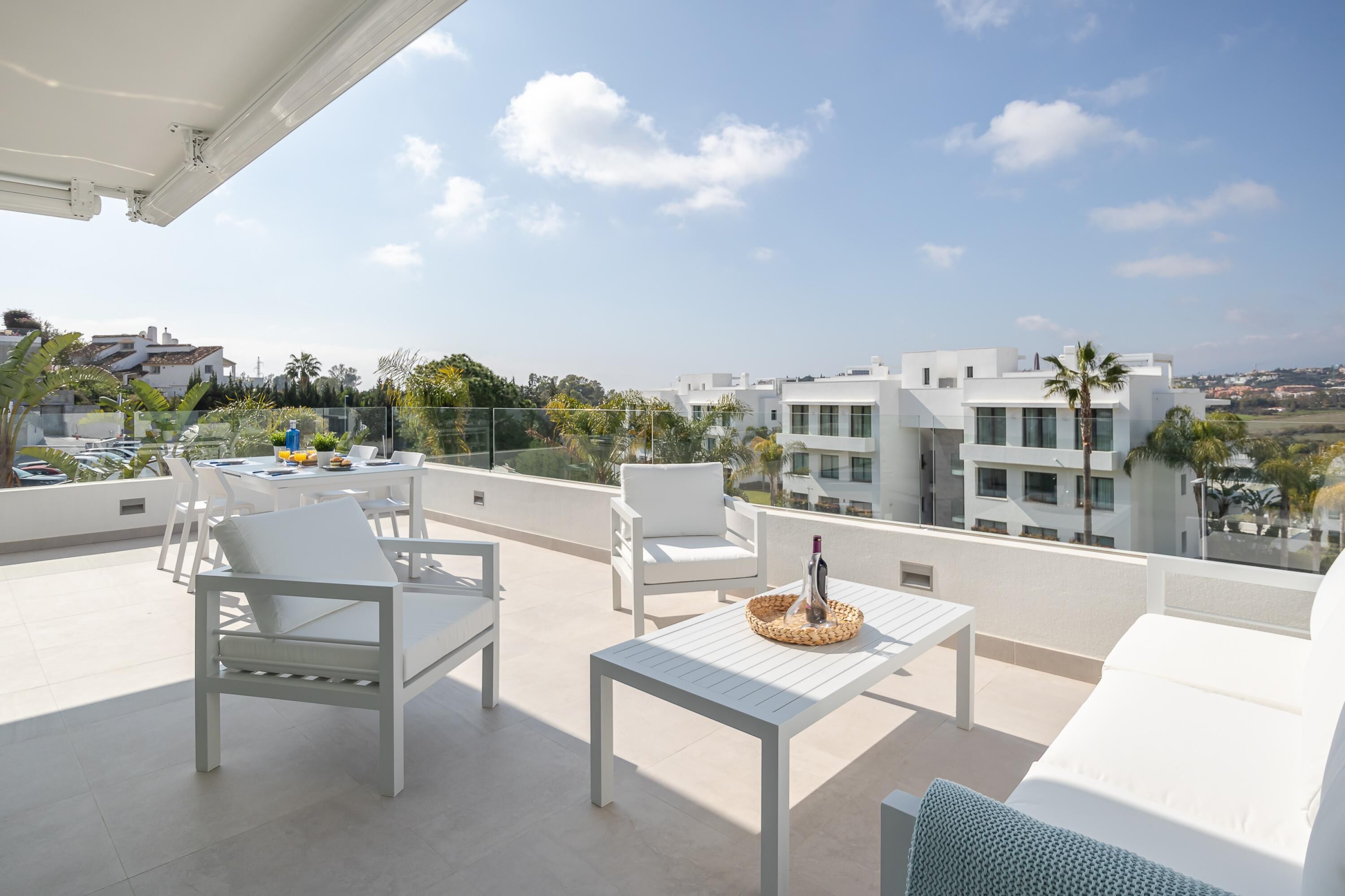 Terraço no telhado com mobiliário branco, incluindo cadeiras e uma mesa, e vista para a paisagem urbana.