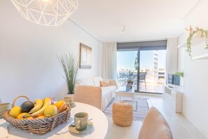 A modern living room with a balcony, a dining area with fruit and coffee, and a sofa. - Sunset Sweet Holidays (Estepona)
