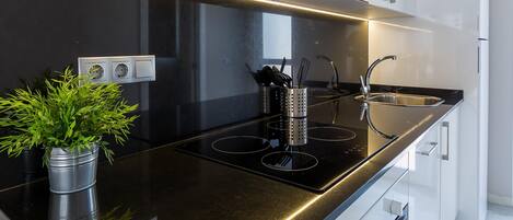 A modern kitchen with a black countertop, stainless steel appliances, and a potted plant.