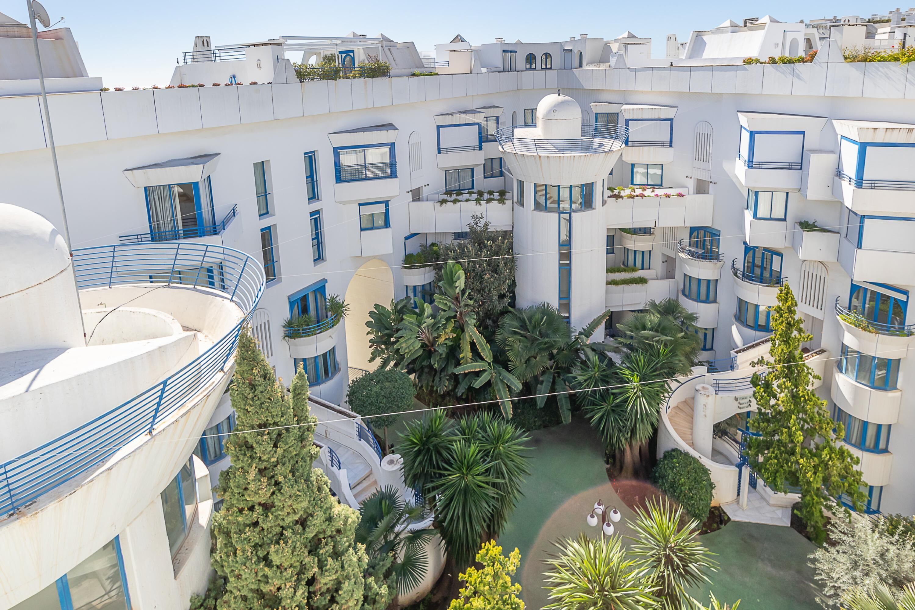 A modern building with multiple balconies, a central courtyard with greenery, and a pool.