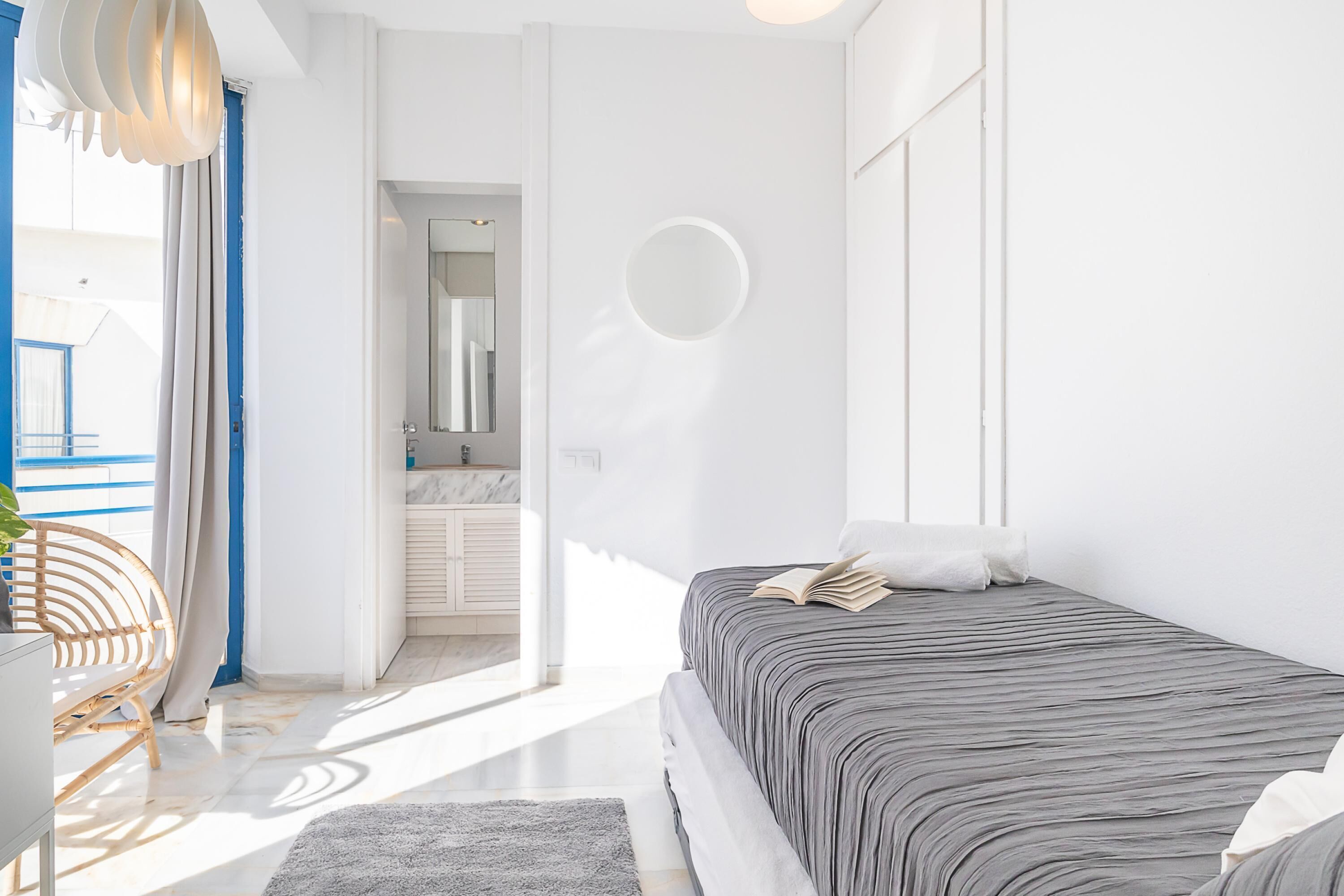 A modern bedroom with a bed, a chair, and a view of the bathroom.