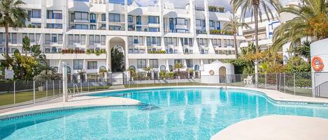 A modern hotel with a pool area, featuring a multi-story building with balconies and a clear blue sky.
