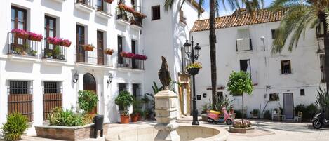 A courtyard with a fountain, white buildings with balconies, and potted plants.