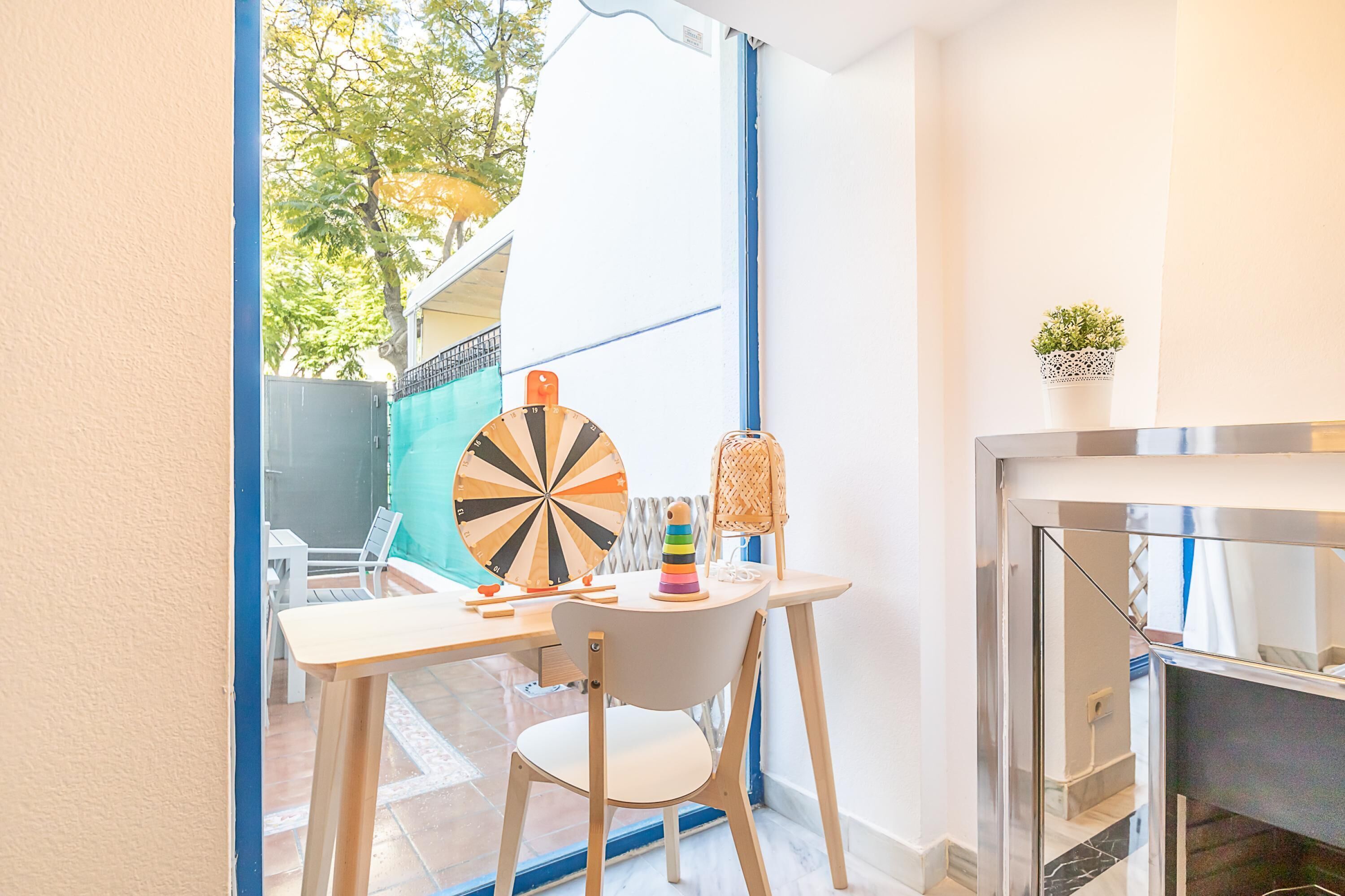 A small, bright room with a table, a chair, a dartboard, and a small plant.