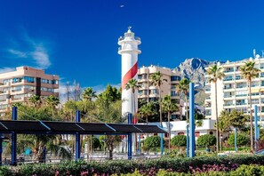 A coastal hotel with a prominent lighthouse, modern buildings, and lush greenery. - Marbella Resort 9 Pool Whirlpool Sauna (Marbella)