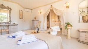 A hotel room with a large bed, a vanity with a mirror, a chair, a dresser, and a small table with towels and a bottle. - Rancho Miraflores Townhouse 2 (Mijas)
