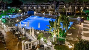 A pool area with lounge chairs and umbrellas, surrounded by a white fence and potted plants.