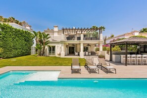 Una casa a due piani con piscina, mobili da esterno e una pergola.