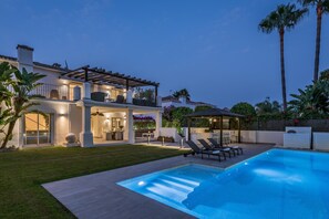 Una casa a due piani con piscina, area salotto esterna e un patio ben illuminato.