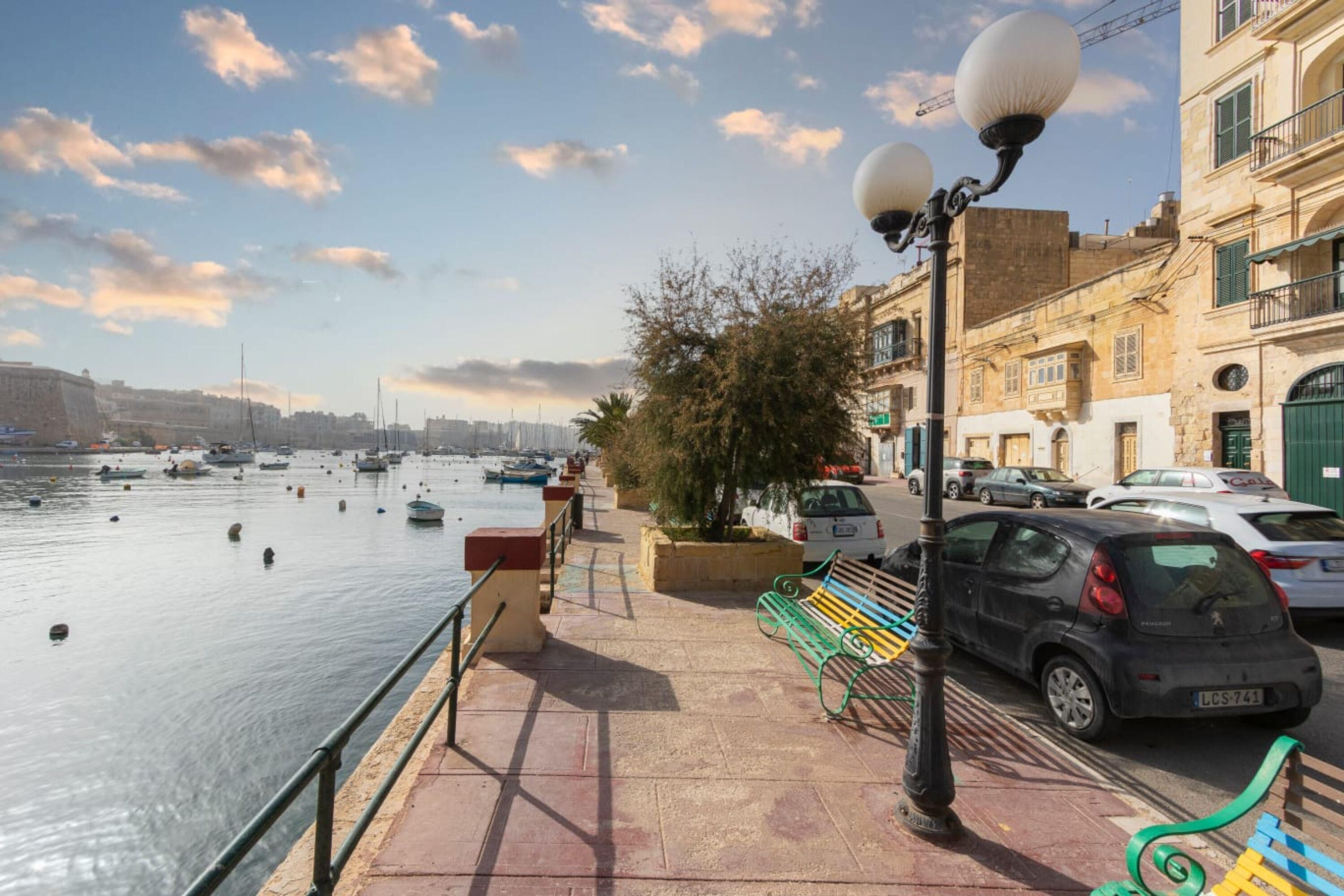 A waterfront promenade with a bench, a lamp post, and parked cars.