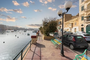 Un paseo marítimo con un banco, un farol y coches estacionados.