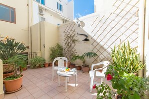 Eine kleine Terrasse mit zwei weißen Stühlen, einem Tisch und verschiedenen Blumentöpfen.