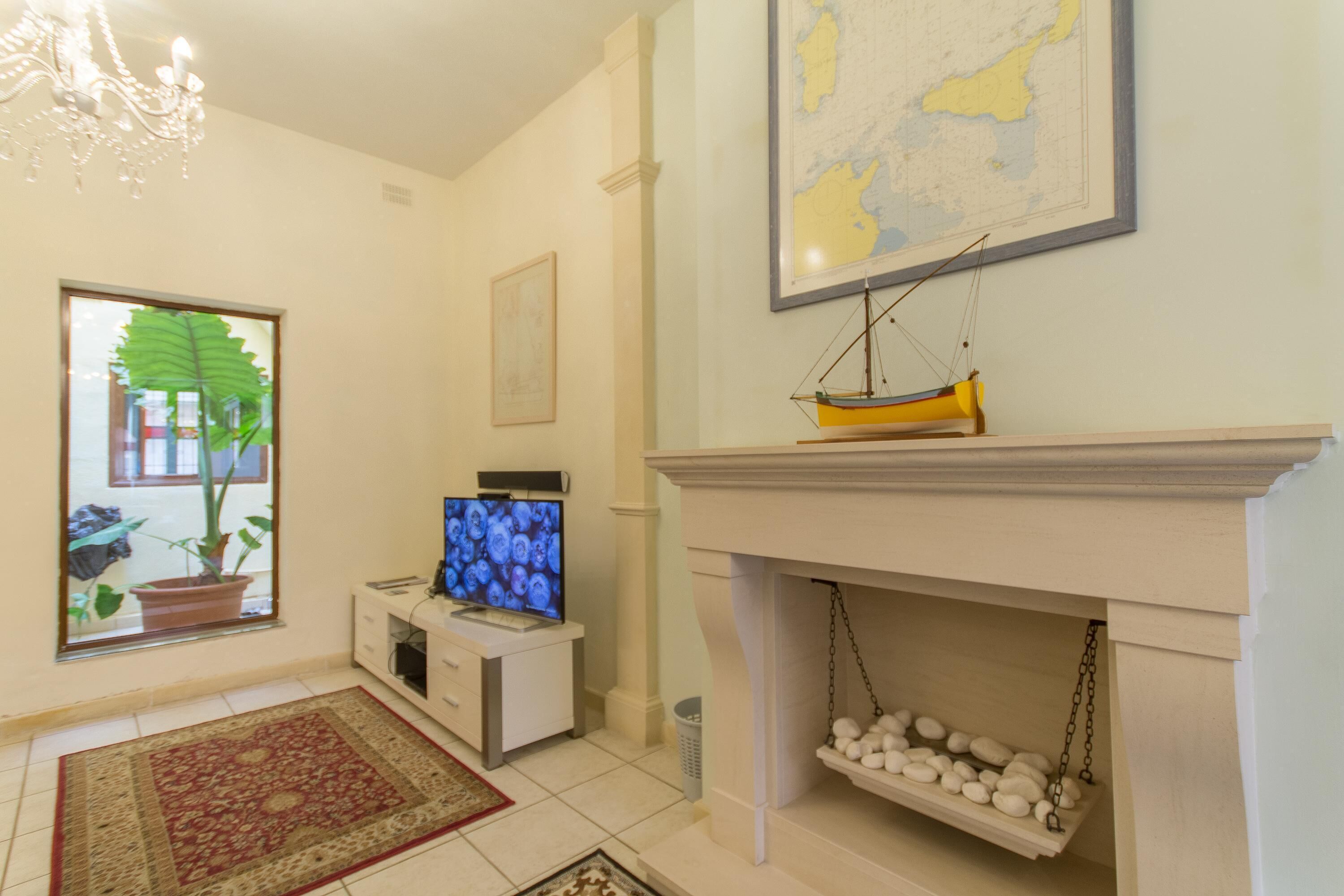 A living room with a television, a fireplace with a hanging shelf, a map on the wall, and a chandelier.