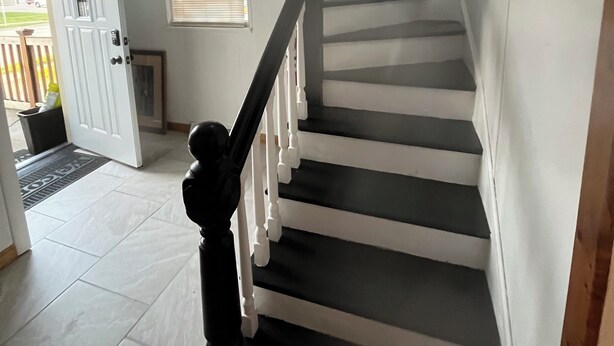 Una escalera con barandas blancas y escalones oscuros, que sube a un piso superior.