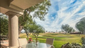 A patio with a round table and chairs, a potted plant, and a view of a golf course.