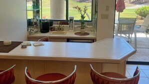 A modern kitchen with a large window, a bar area with red stools, and a 'Hello Sunshine' sign.