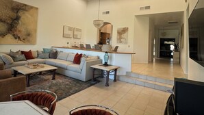 A spacious living room with a high ceiling, skylights, a large sofa, a coffee table, and a dining area.