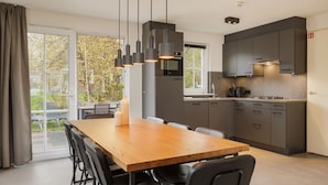 A modern kitchen with a wooden dining table and chairs, grey cabinets, and pendant lighting. - Home w/ Sauna & Garden (Bad Bentheim)