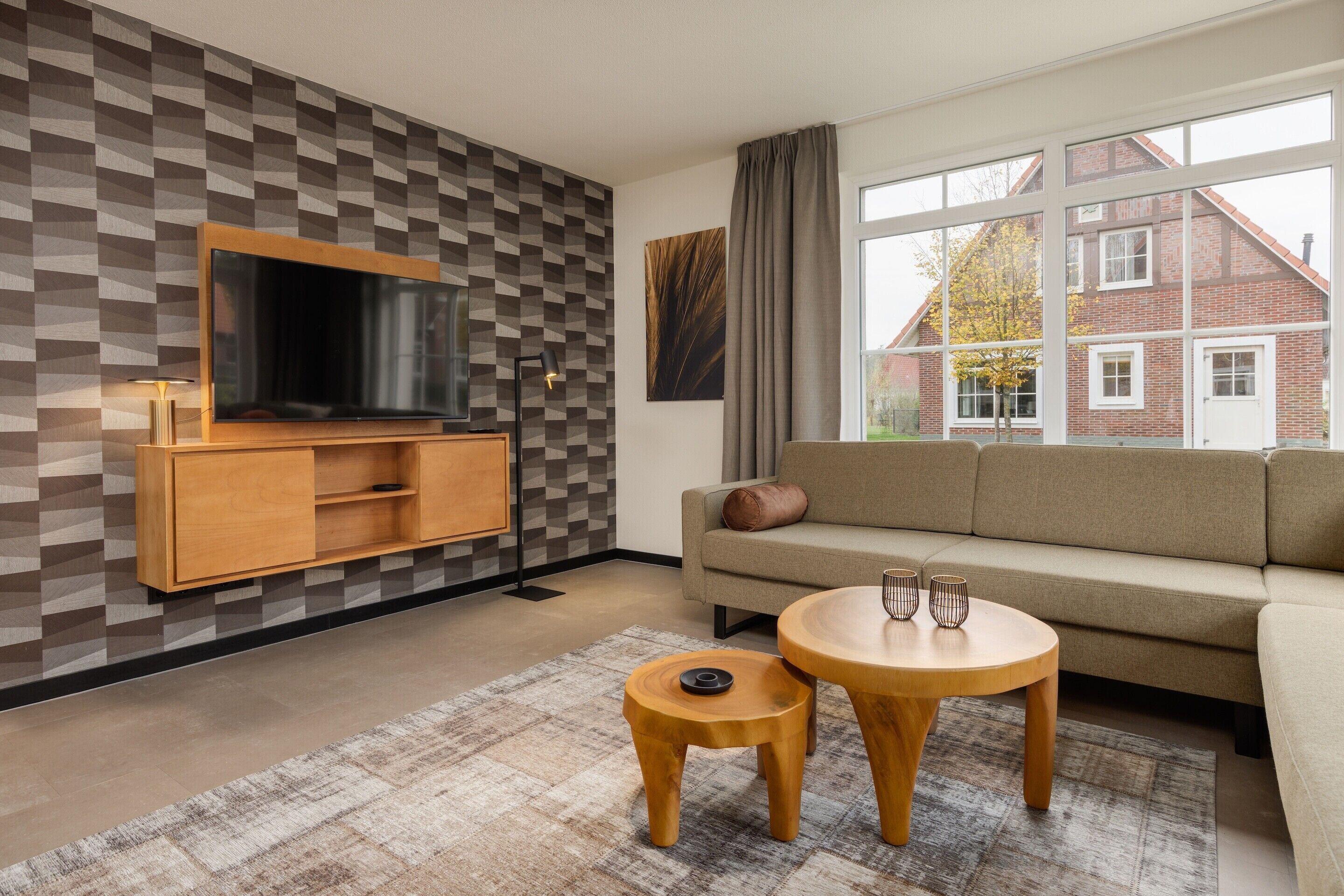 A modern living room with a TV, sofa, two wooden tables, and a patterned wall.