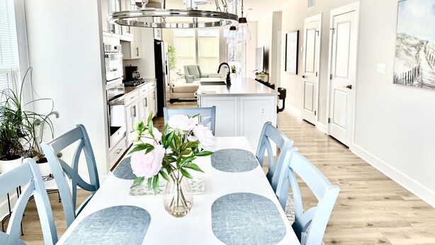 A modern kitchen with white cabinets, a central island, and a dining area with a white table and blue chairs.