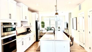 A modern kitchen with white cabinetry, stainless steel appliances, a central island, and a pendant light.