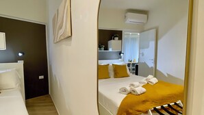 Una camera d'albergo con un grande specchio, un letto con una coperta gialla, una sedia bianca e un tavolino con una pianta.