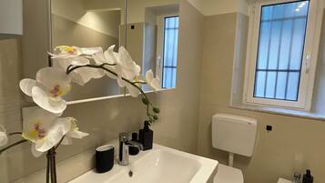 A modern bathroom with a white sink, a black cup, a mirror, and white orchids.