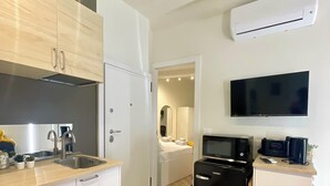 Una cucina compatta con mobili bianchi, forno a microonde integrato e frigorifero nero.
