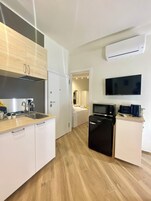 Una cocina compacta con muebles blancos, un microondas integrado y un refrigerador negro.