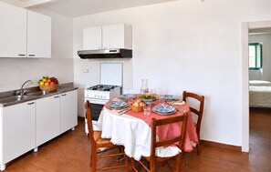 A compact kitchen with white cabinets, a gas stove, and a dining table set for four with a red tablecloth. - 1 bedroom lovely apartment in Longobardi (Longobardi)