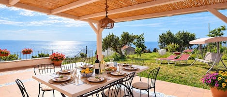 Un'area pranzo all'aperto coperta, con un tavolo apparecchiato per quattro persone, con vista panoramica sul mare.
