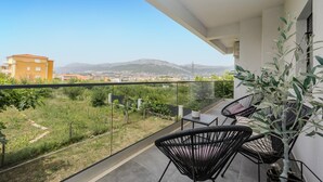 Un balcon doté d’une balustrade en verre, de deux fauteuils en osier noir et d’une plante en pot.