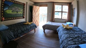 A room with two beds, a wooden floor, a large painting on the wall, and a window with curtains. - Salkantay Hostel Chaullay (Santa Teresa)