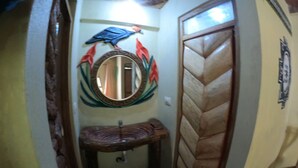 A narrow hallway with a wooden door, a mirror with a decorative frame, and a small sink with a curved basin. - Salkantay Hostel Chaullay (Santa Teresa)